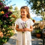 Κορίτσι με λευκό πλεκτό ζακετάκι LUCIA σε εξωτερικό χώρο με λουλούδια