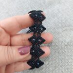 Κοντινή λήψη μαύρου macrame βραχιολιού με γεωμετρικό μοτίβο και μαύρα κρύσταλλα στο χέρι